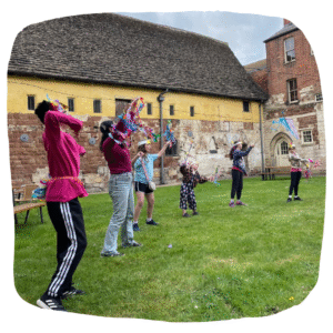 Colour photo of young people dancing on a grass field, surrounded by old priory building
