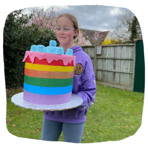 Colour photo of young person carrying a large multi-coloured crafted cake!